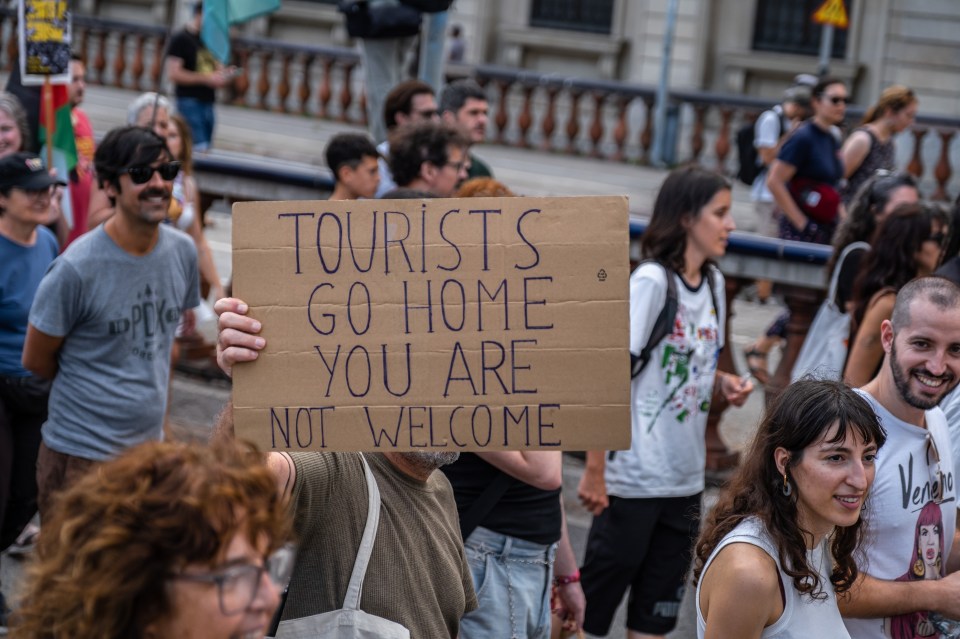 Protestor holding a sign that reads "Tourists go home you are not welcome."