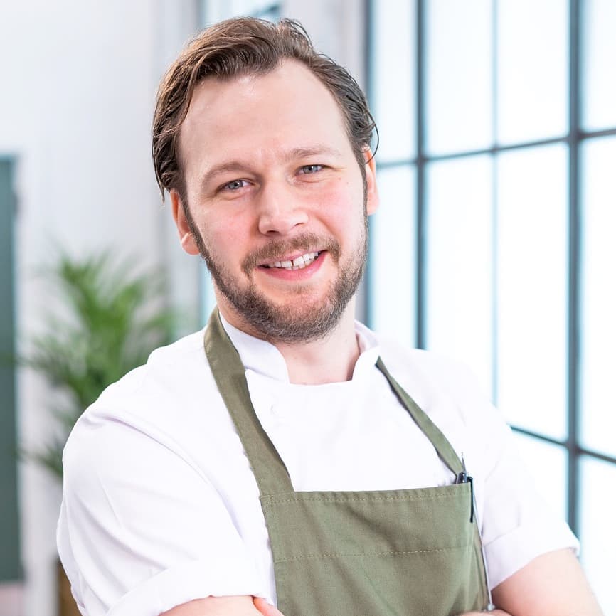 Portrait of a smiling chef in a white shirt and green apron.