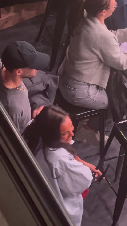 Ruben Dias and Maya Jama cuddling and kissing while watching a football match.