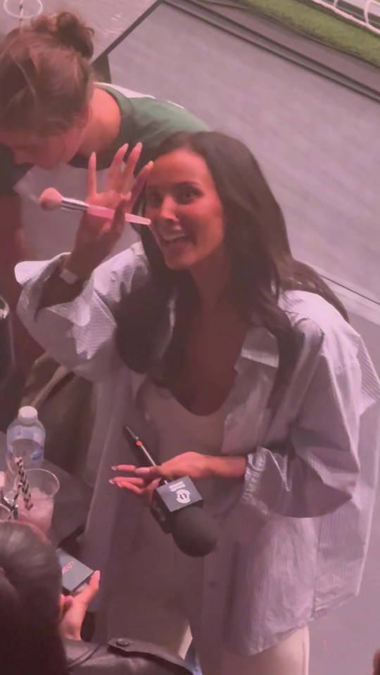 Maya Jama holding a makeup brush and microphone during an interview.