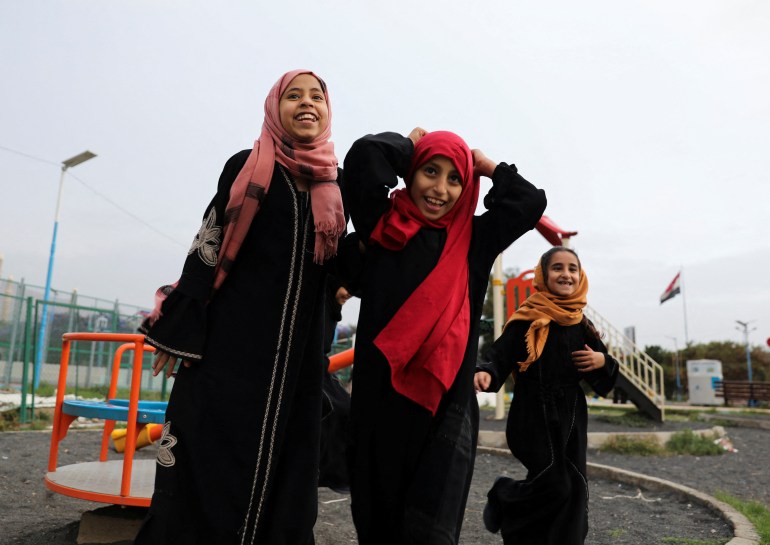 Three little girls in black robes and red hijabs playing in a park