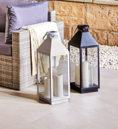 Two lanterns with candles, next to patio furniture.