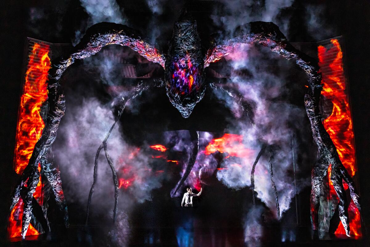 A person is dwarfed by a giant spider-like creature onstage