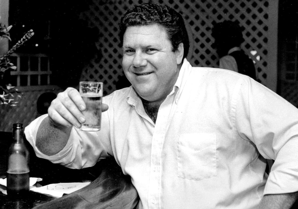 A black and white photo of a man holding a glass of beer with his right hand.