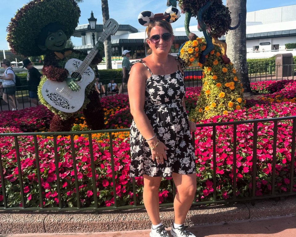 Woman in floral dress at Disney in front of floral topiaries.