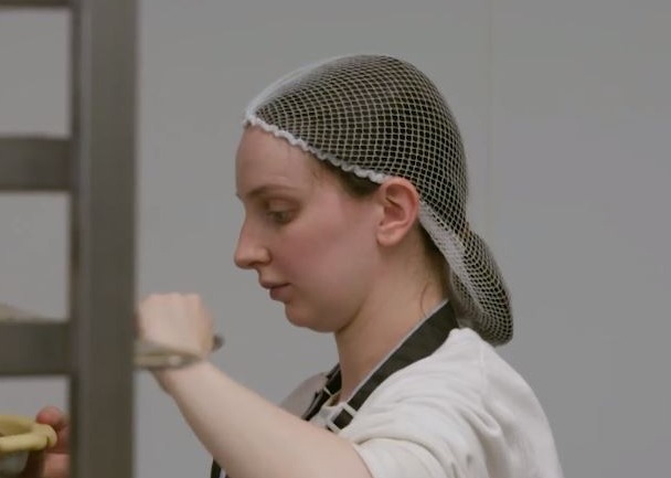 A woman wearing a hairnet prepares food.