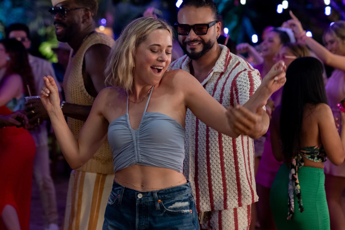 A woman in a halter crop top and jean shorts on the dance floor as a man touches her arm.
