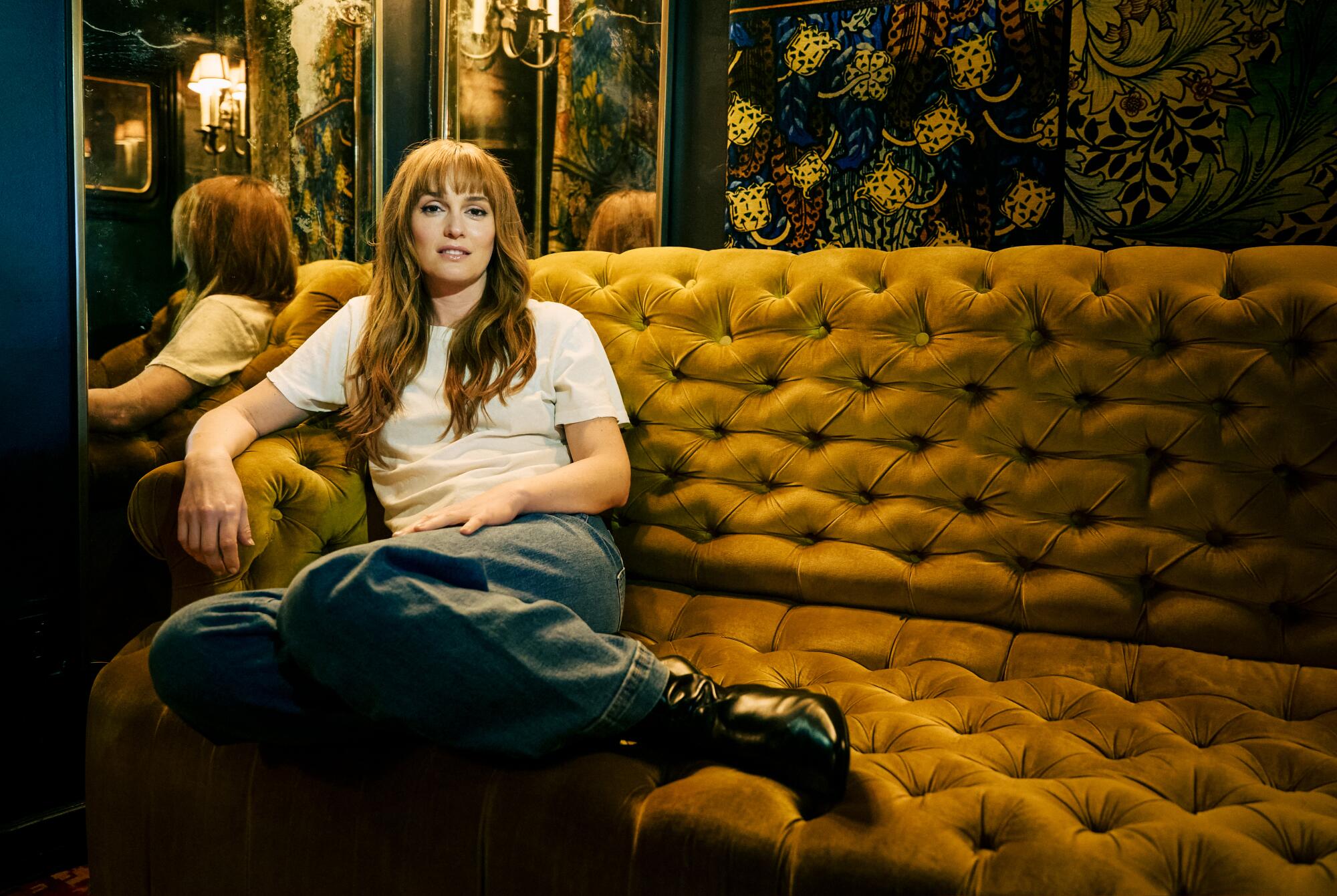 A woman with long hair sits casually, legs up, on a gold quilted sofa