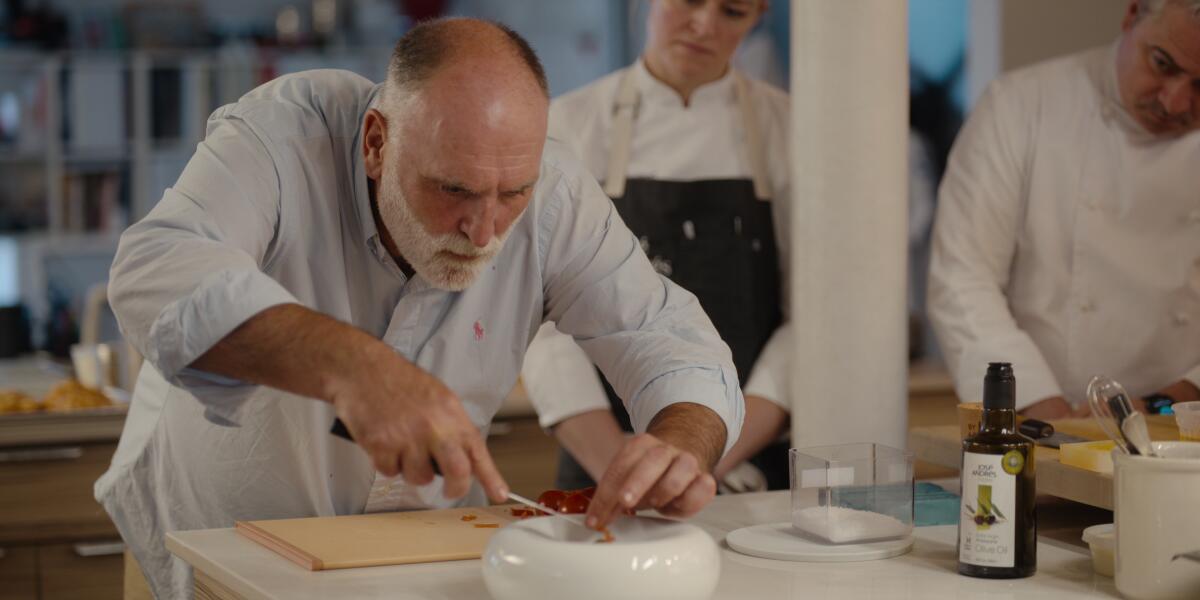 A balding man delicately places a garnish on a white bowl.