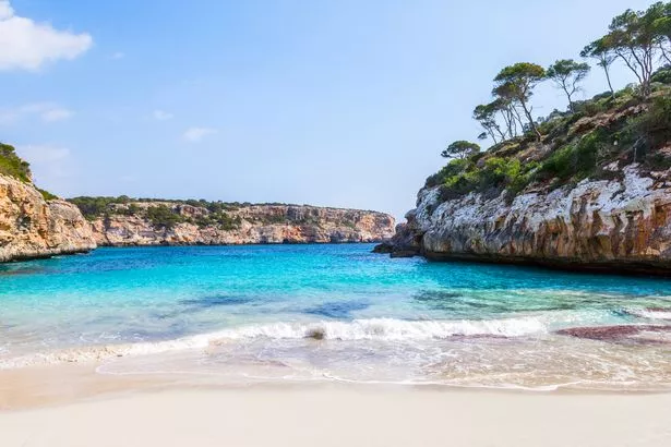 Image of Calo des Moro beach completely empty, with water and cliffs in distance