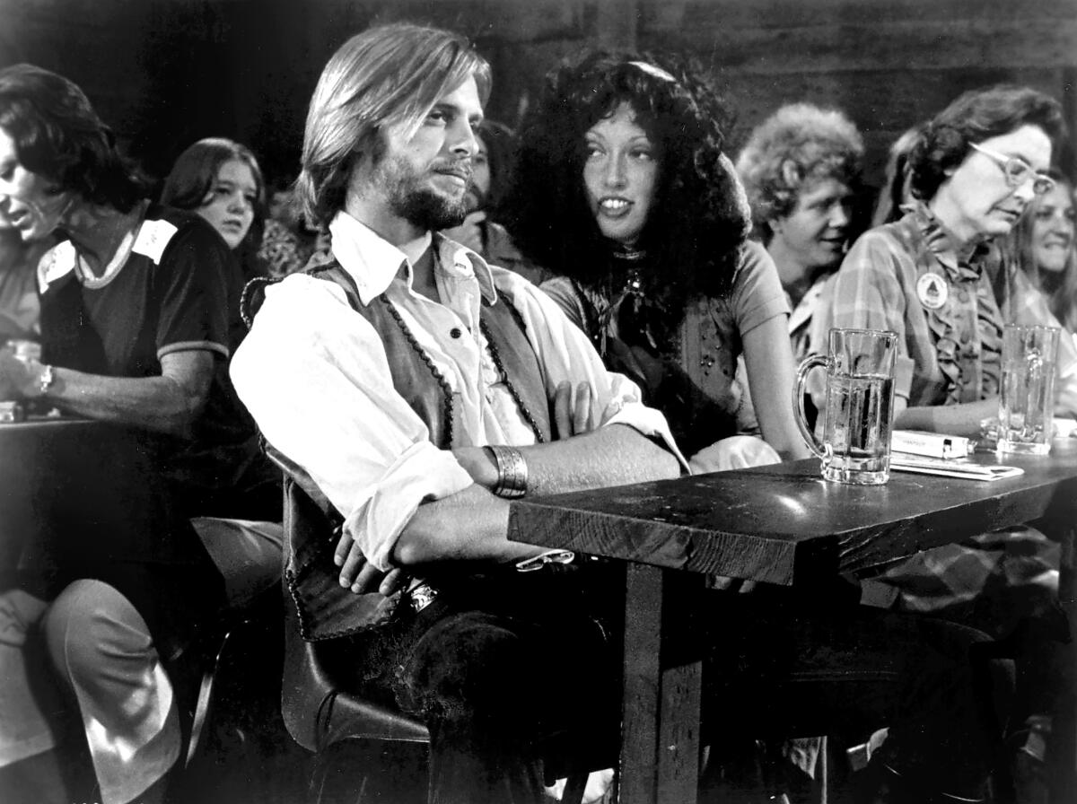 A man and a woman sit at a table in a bar, watching live music.