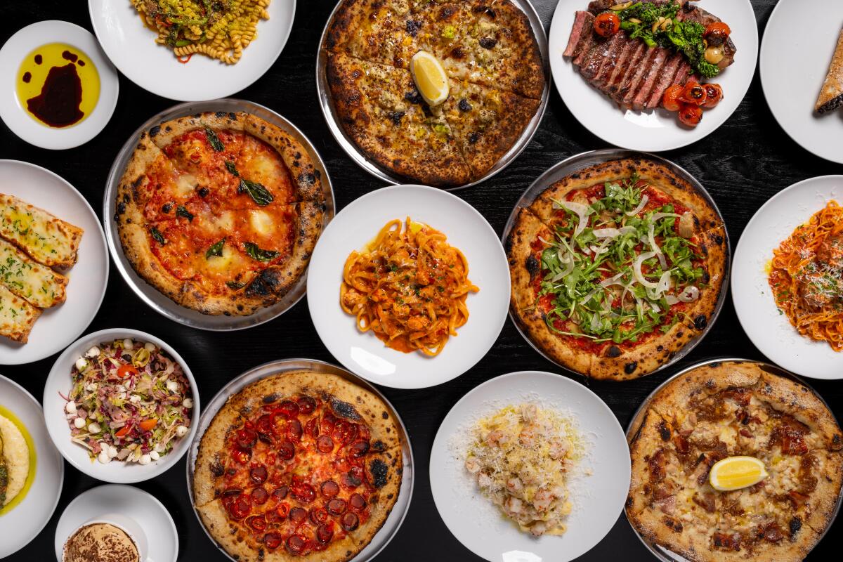 An array of pizza and dishes on a black table at Downtown Dough.