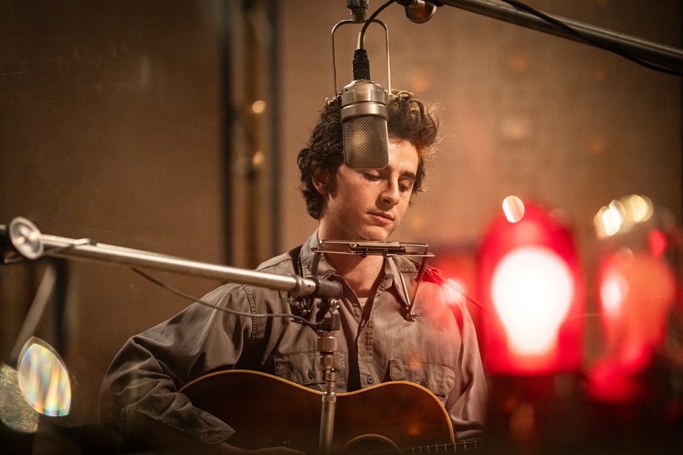 Timothée Chalamet playing guitar and harmonica in a recording studio.
