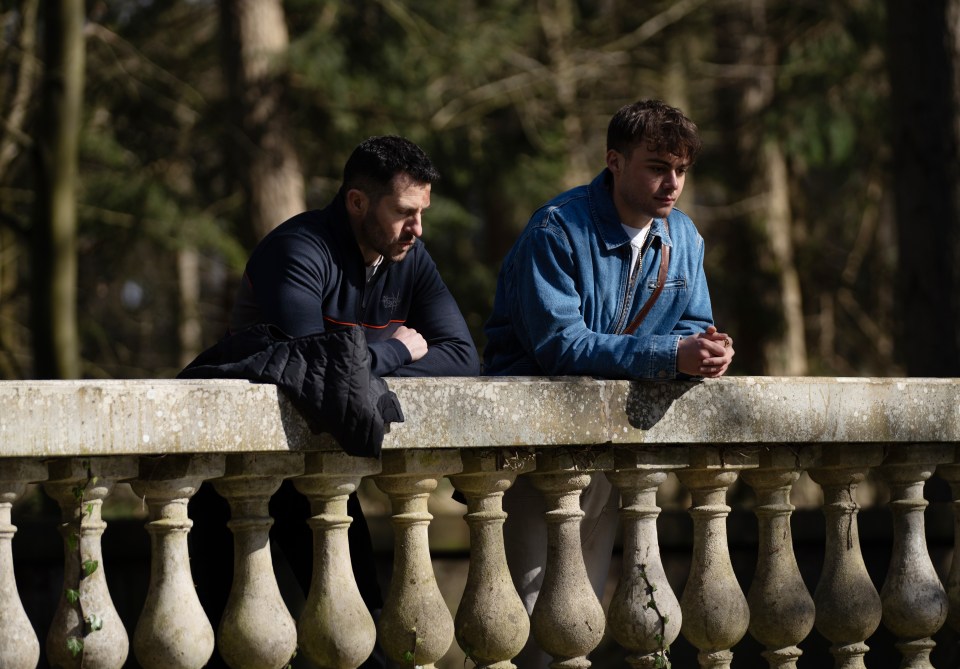 Two men leaning on a stone balustrade in a wooded area.