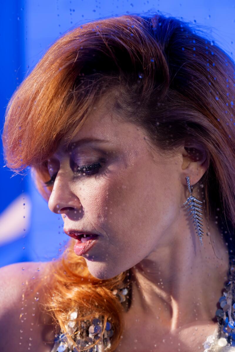 A redheaded woman looks downward with her eyes shut.