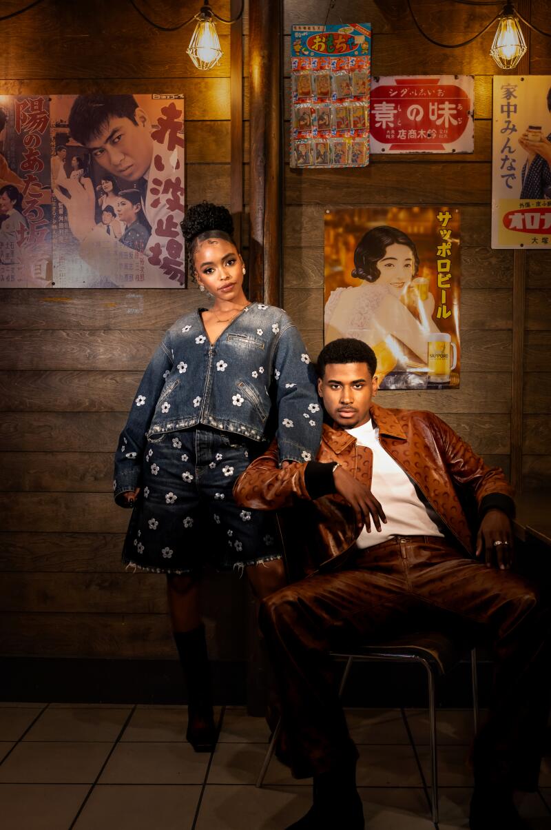 A woman in a matching jean outfit and a man in a brown leather ensemble pose for a photo