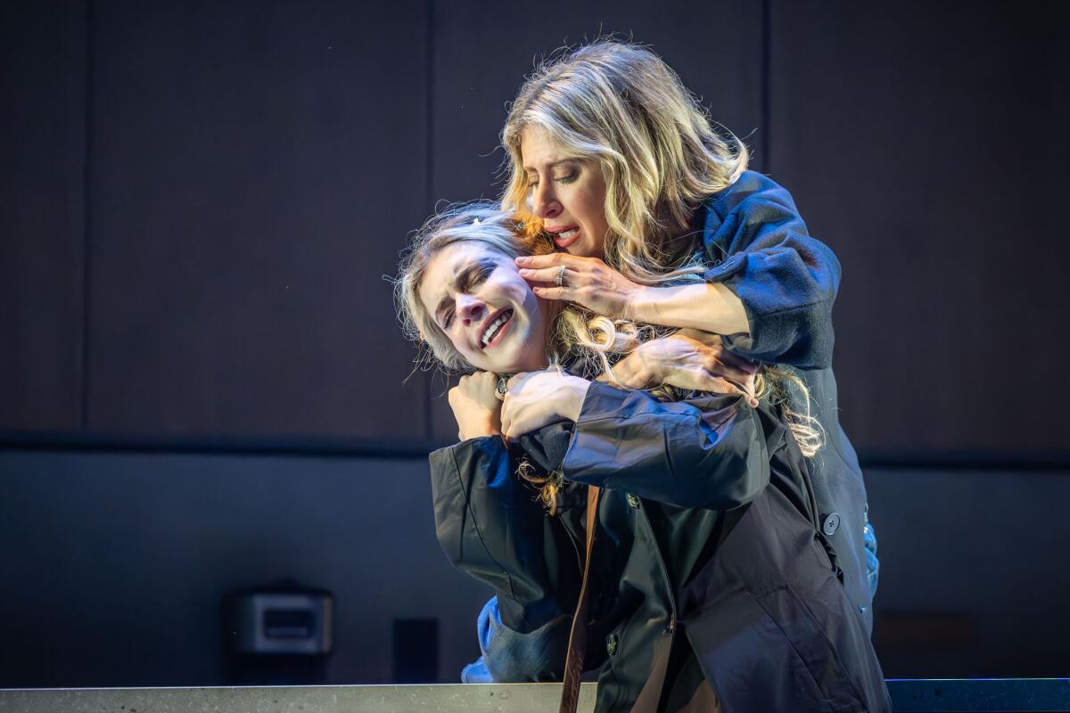 A woman embraces another woman from behind while stroking her cheek.