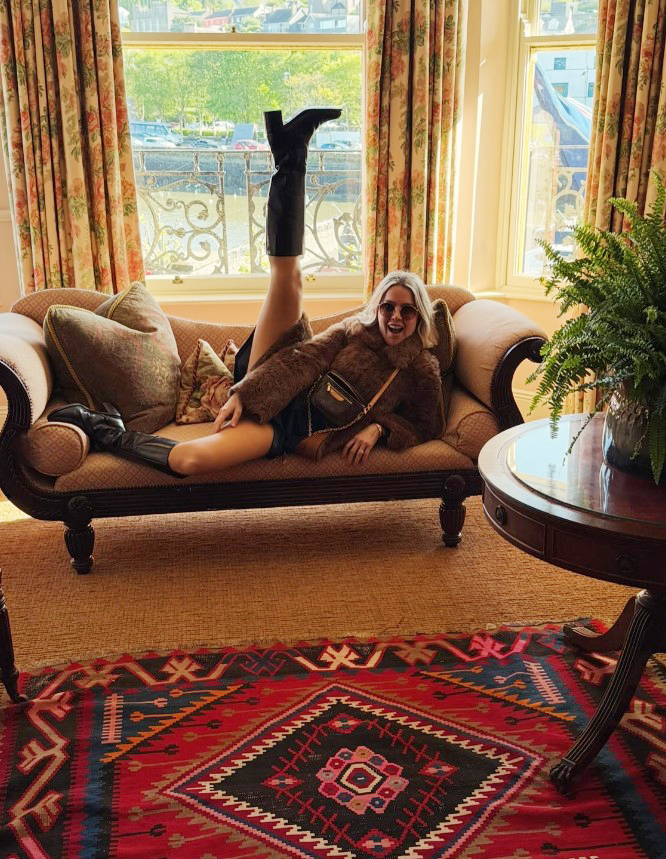Woman in brown fur coat and boots lounging on a chaise lounge.