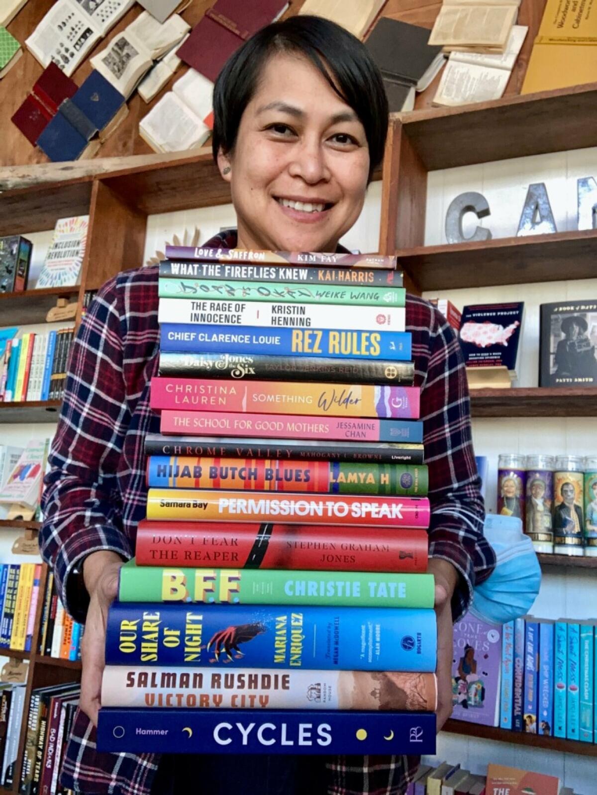 A person holds a stack of books in front of a shelf