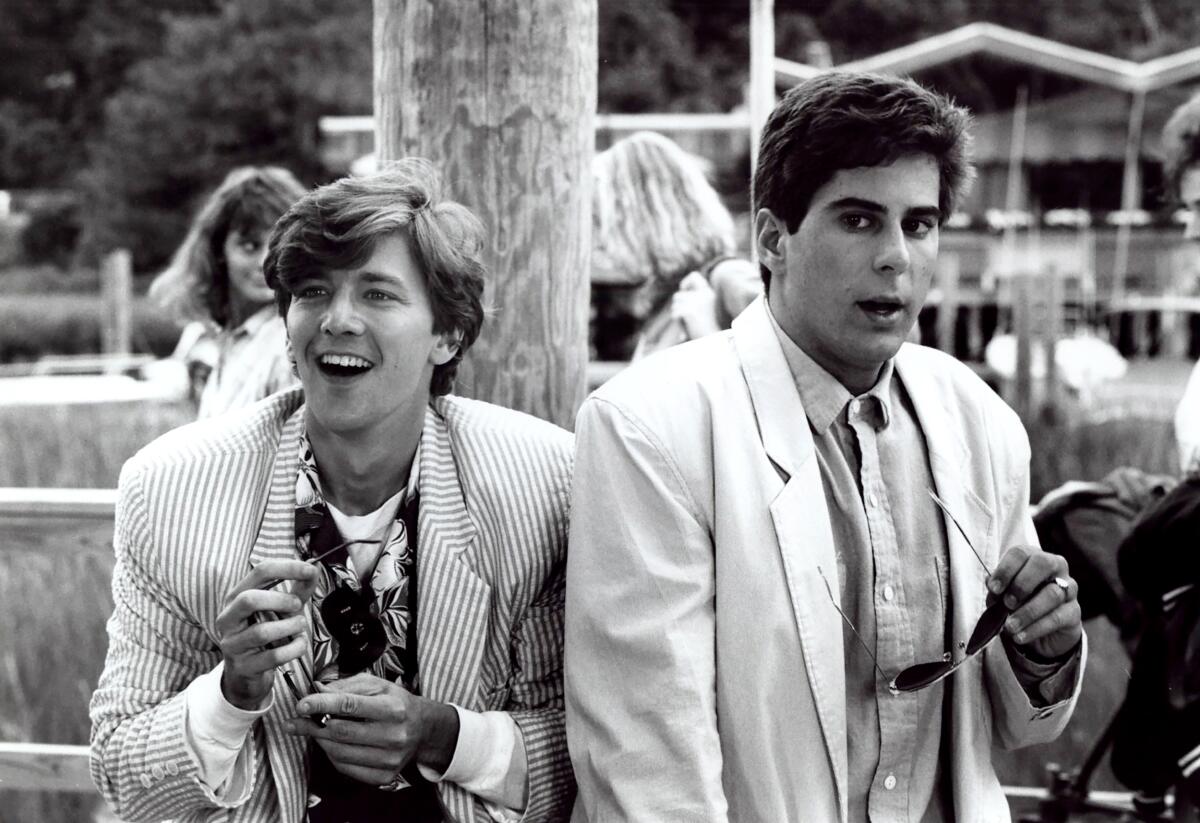 Two men in white suits laugh at a party.