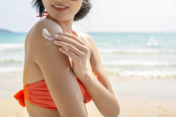 Young woman with sun shape on the shoulder holding sun cream bottle on the beach