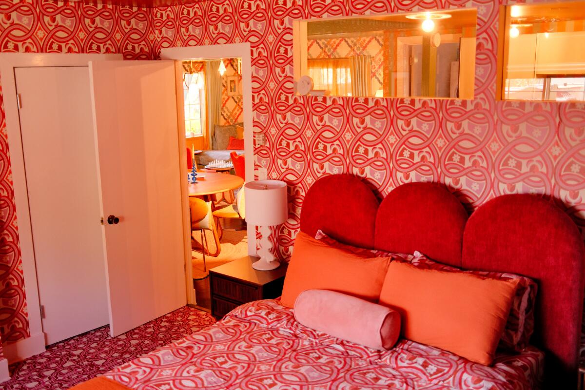 A bedroom with red and orange print wallpaper and bedding