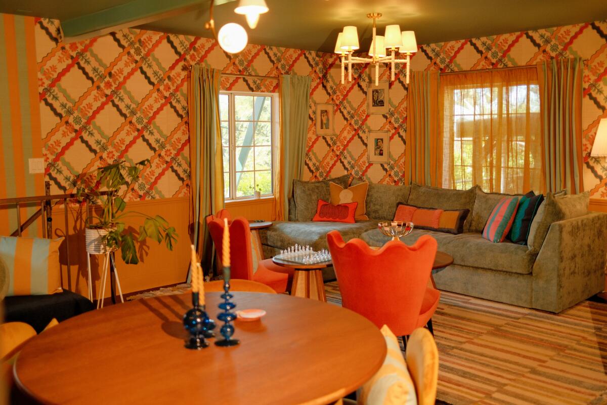 A living room with a blue velvet sofa, dining table and plaid wallpaper