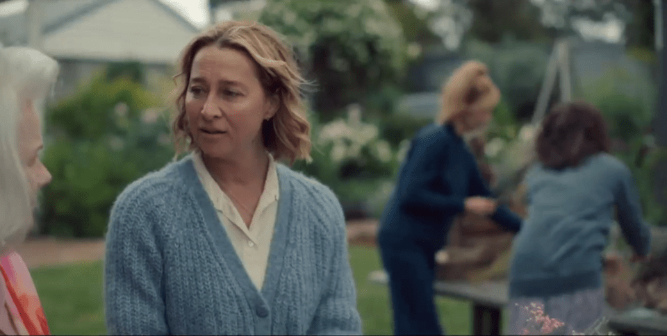 Screenshot of a woman in a blue cardigan talking to an older woman in a garden.