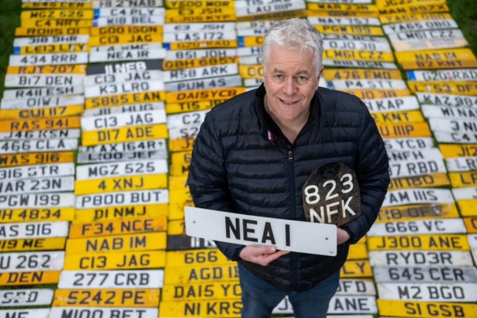 Man holding a number plate, surrounded by hundreds of other number plates.
