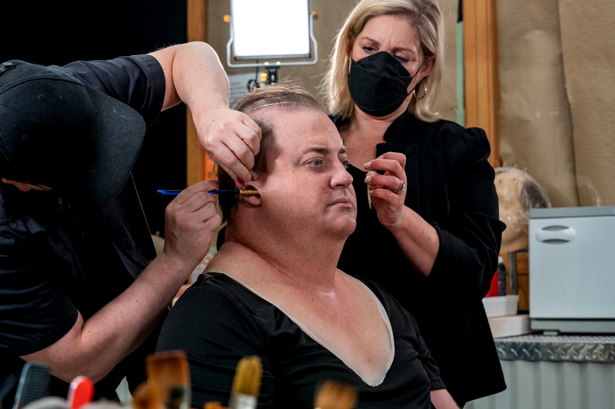 Designers and stylists apply makeup and prosthetics to an actor's face.