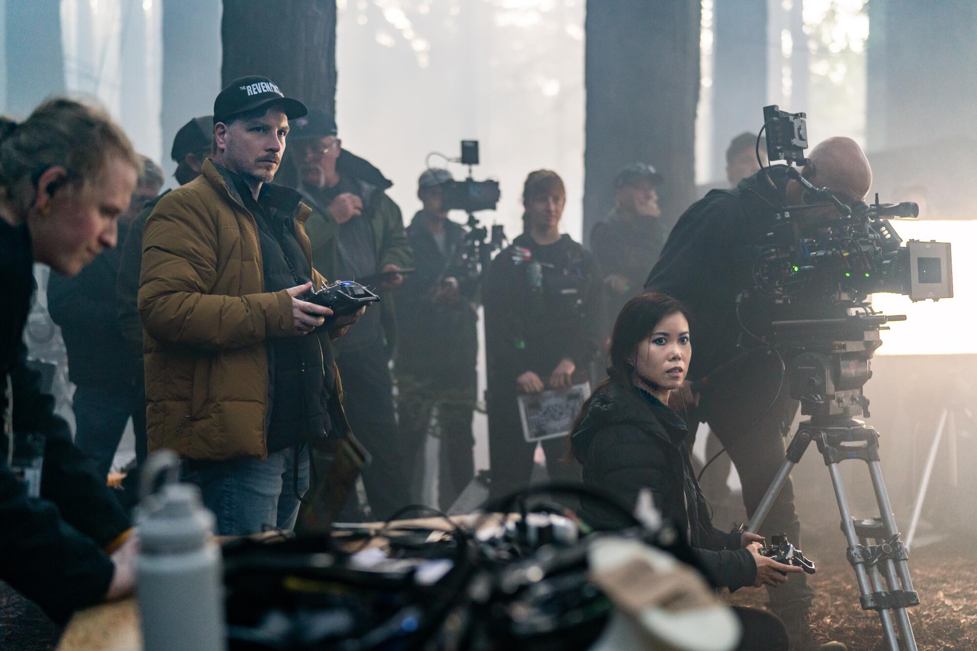 Two makeup artists operate an animatronic robot in a forest set.