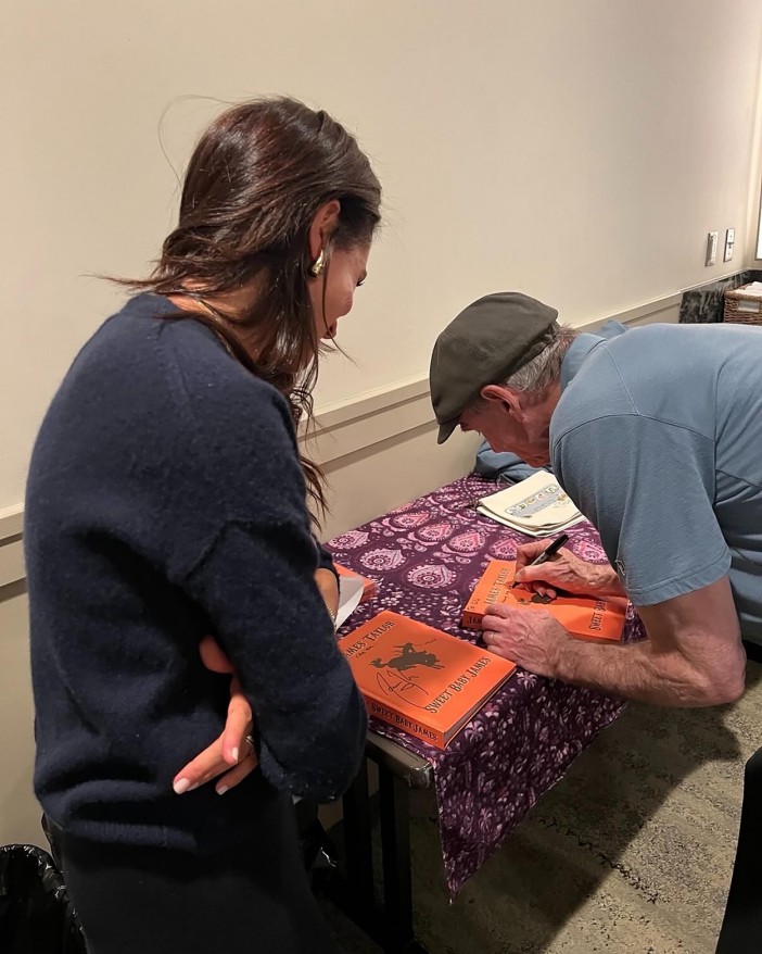 Meghan Markle watching James Taylor sign a book.