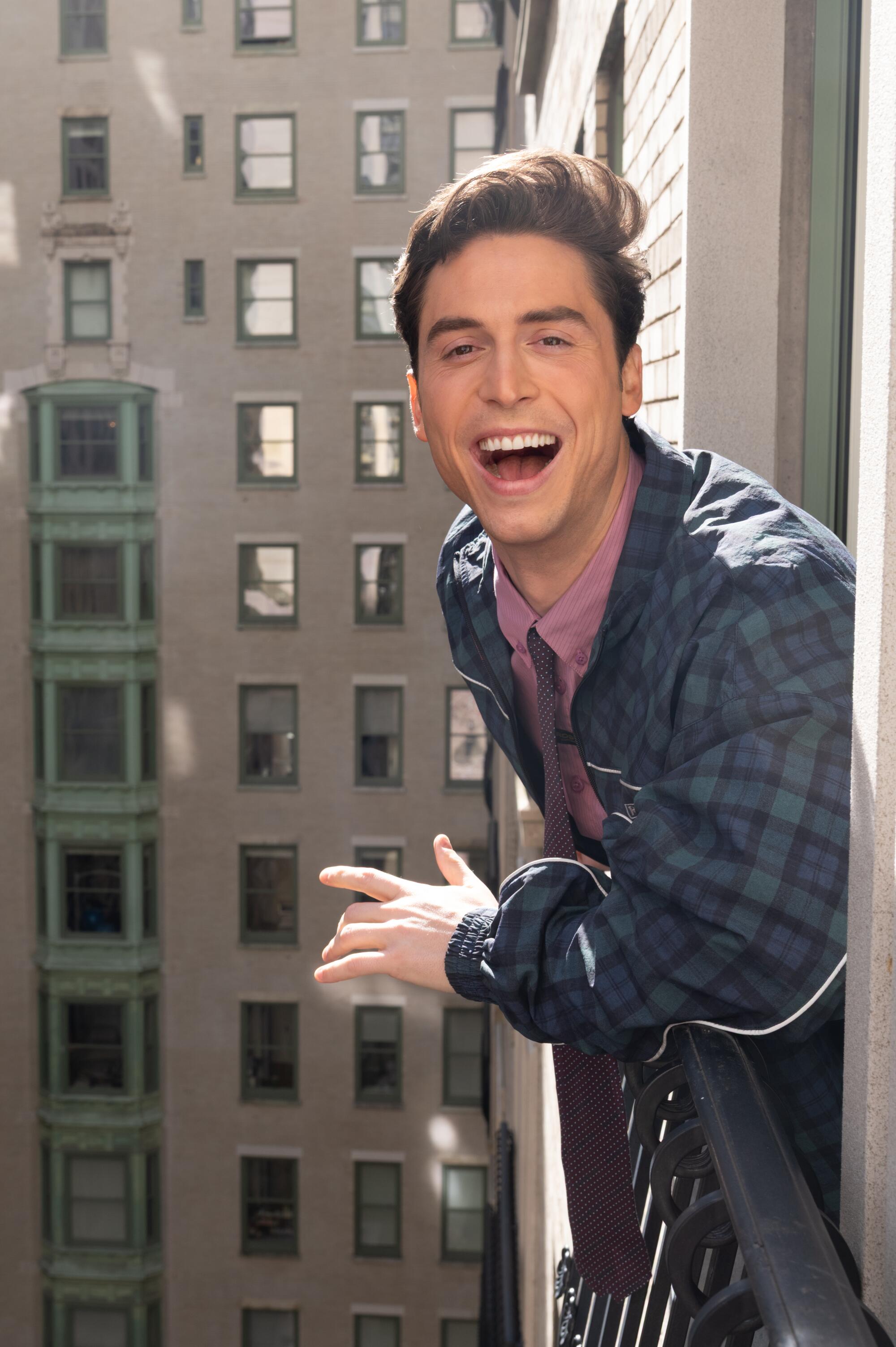 A man in a green plaid jacket smiles wide as he leans against the railing of a window.