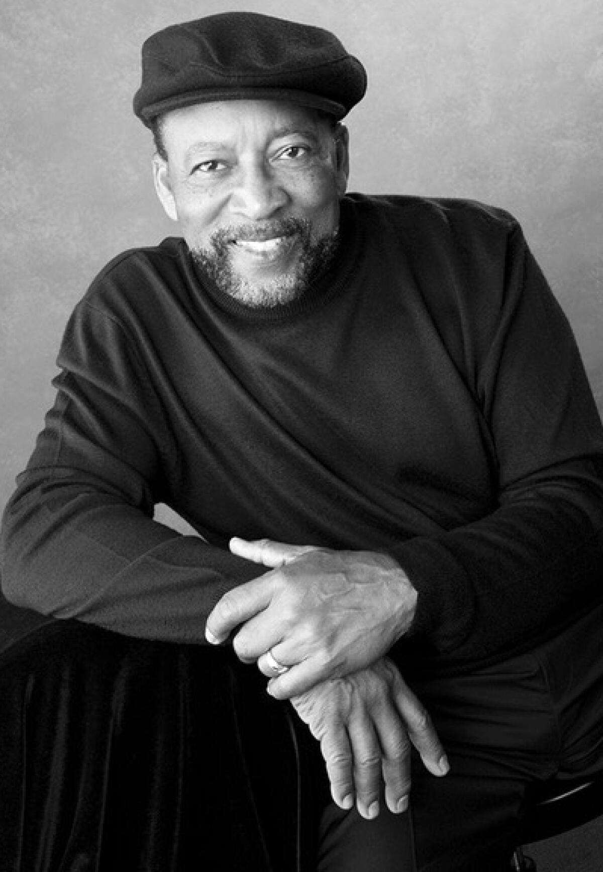 Charles A. Bibbs, in a beret and turtleneck sweater, holds his wrist.