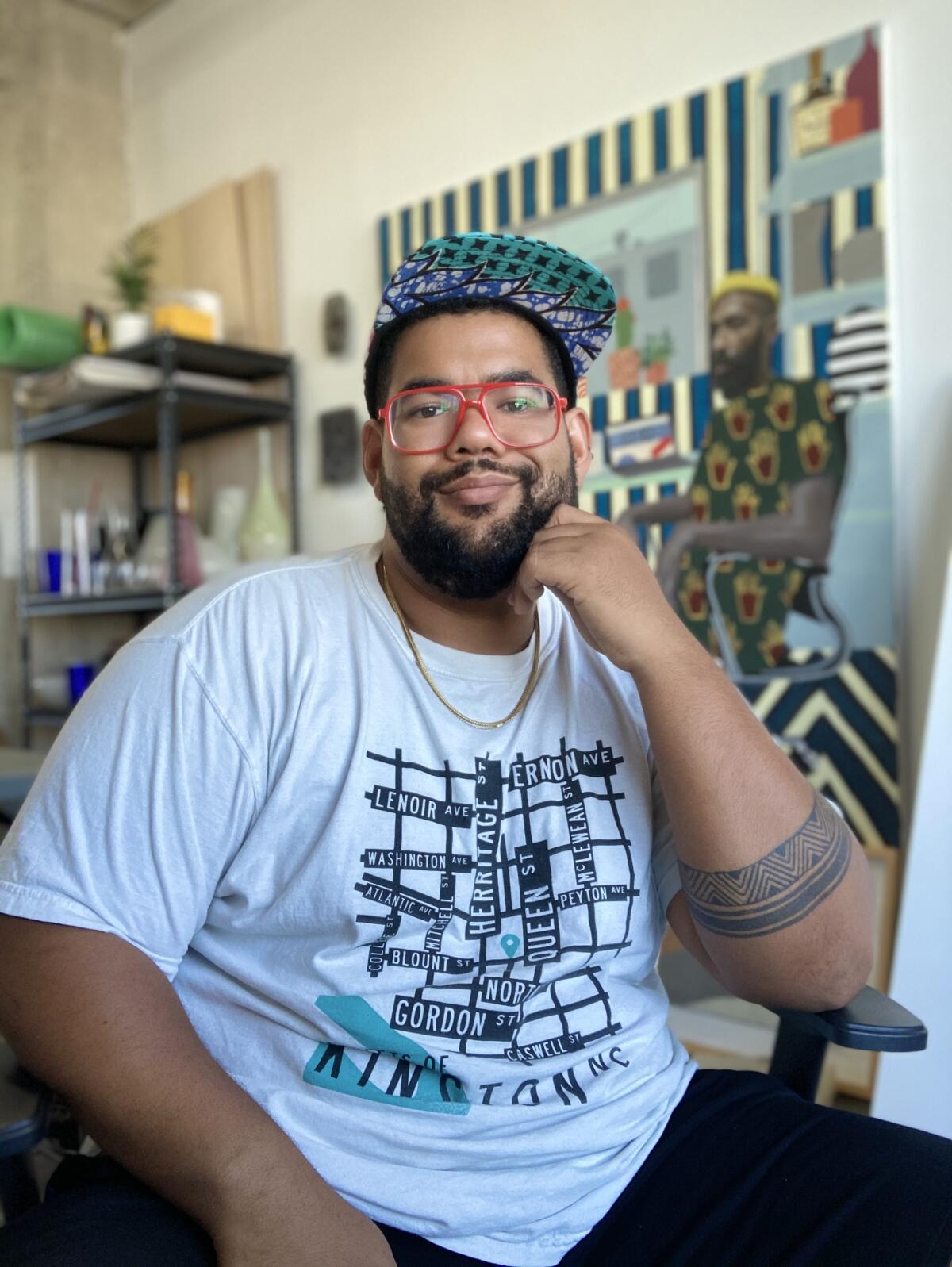 Corey Pemberton, with a cap and white T-shirt decorated with street signs, rests his fist under his chin.