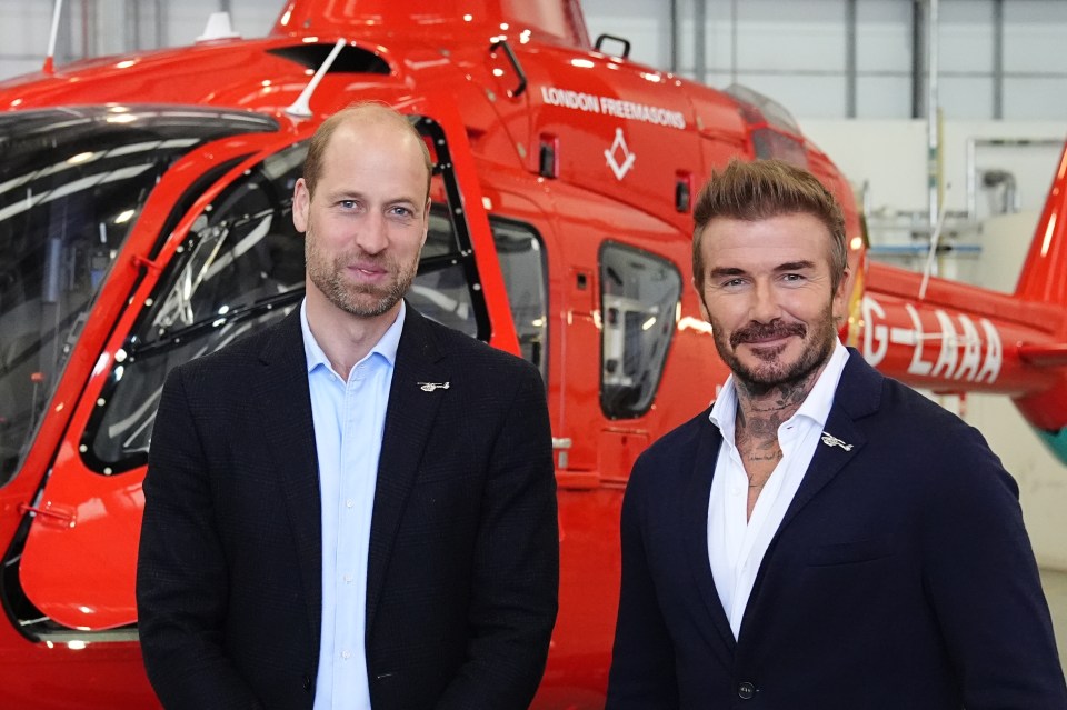 Prince William and David Beckham stand in front of a London Air Ambulance helicopter.