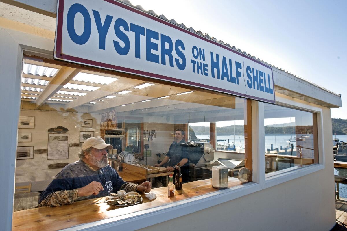 A man enjoys a platter of a half dozen barbecue oysters inside a restaurant.