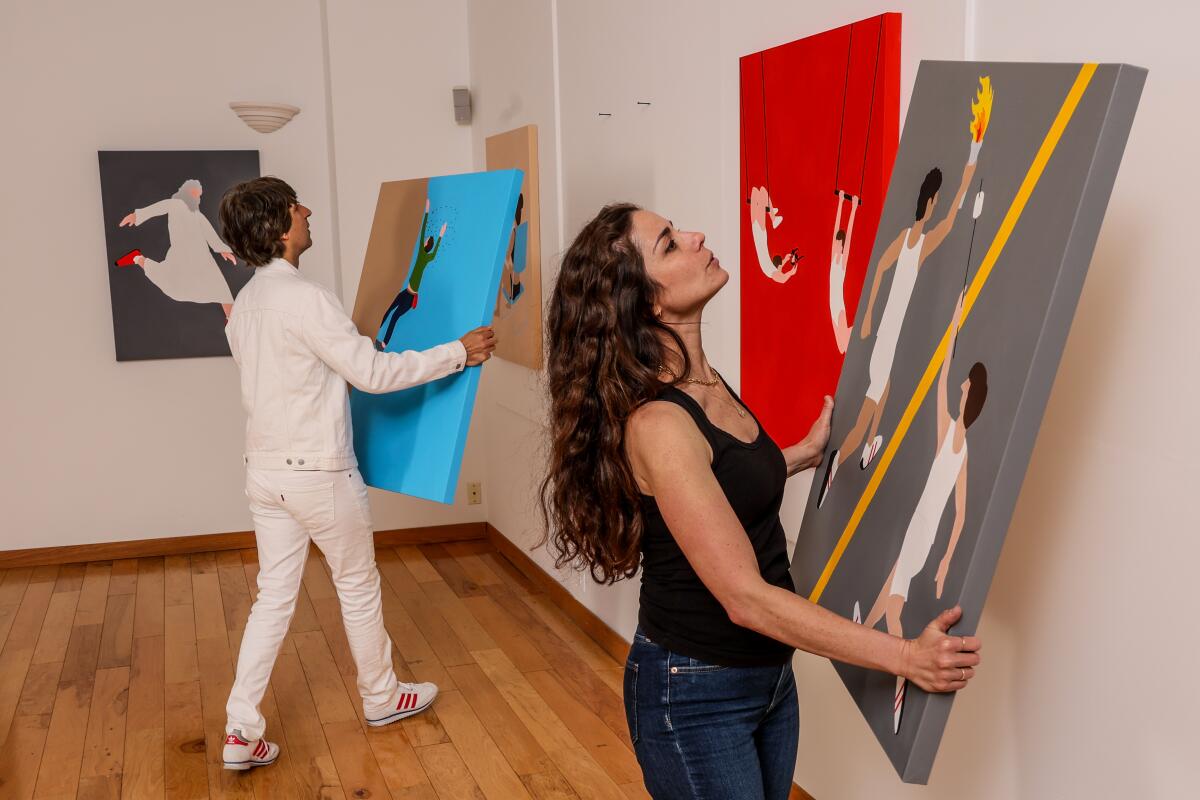 Demetri Martin and Rachael Beame Martin hang art on a gallery wall.
