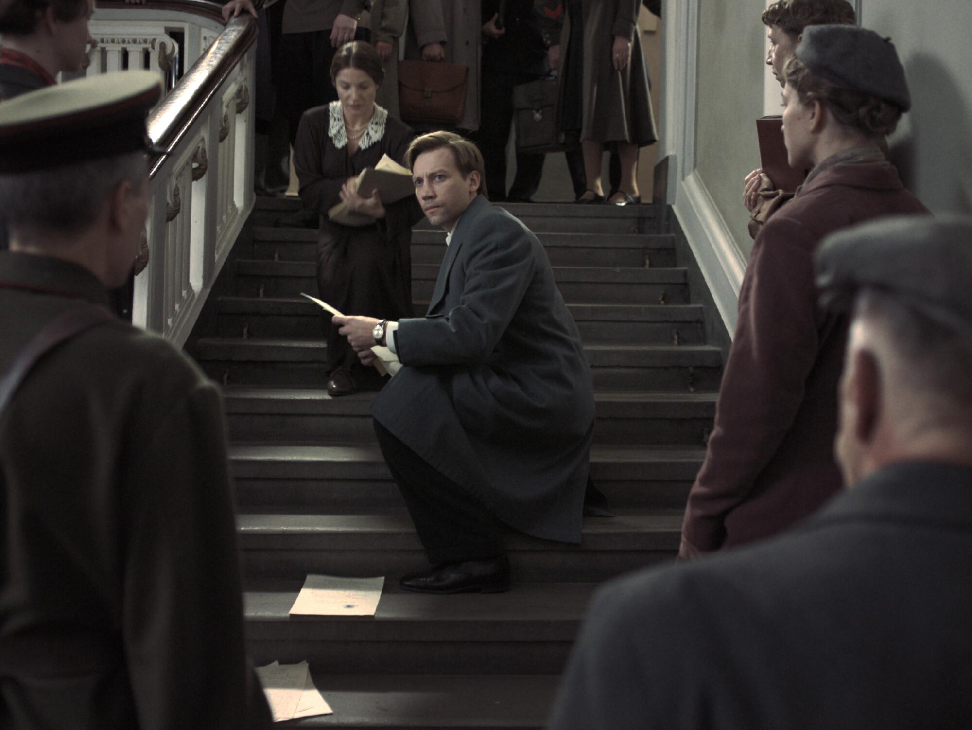 A young lawyer picks up papers on a Soviet-era stairway.
