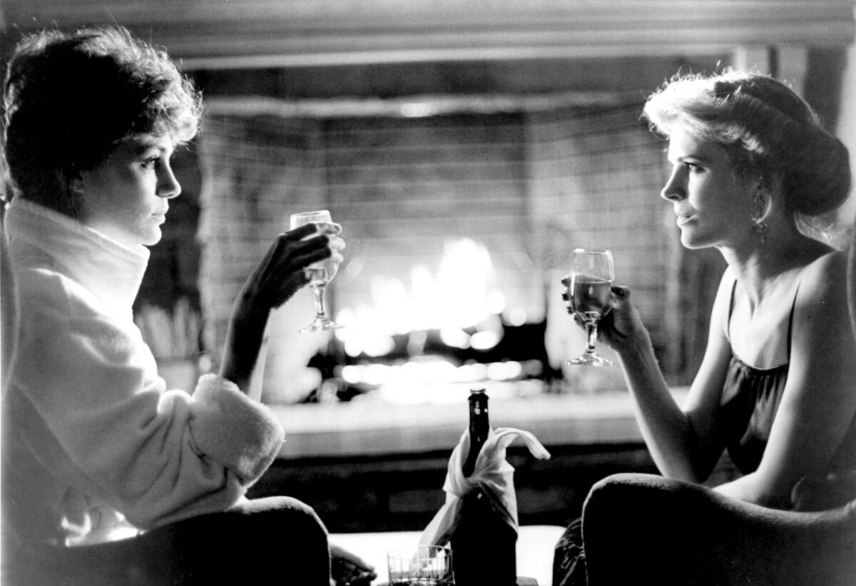 Two women share some Champagne in front of a roaring fire.
