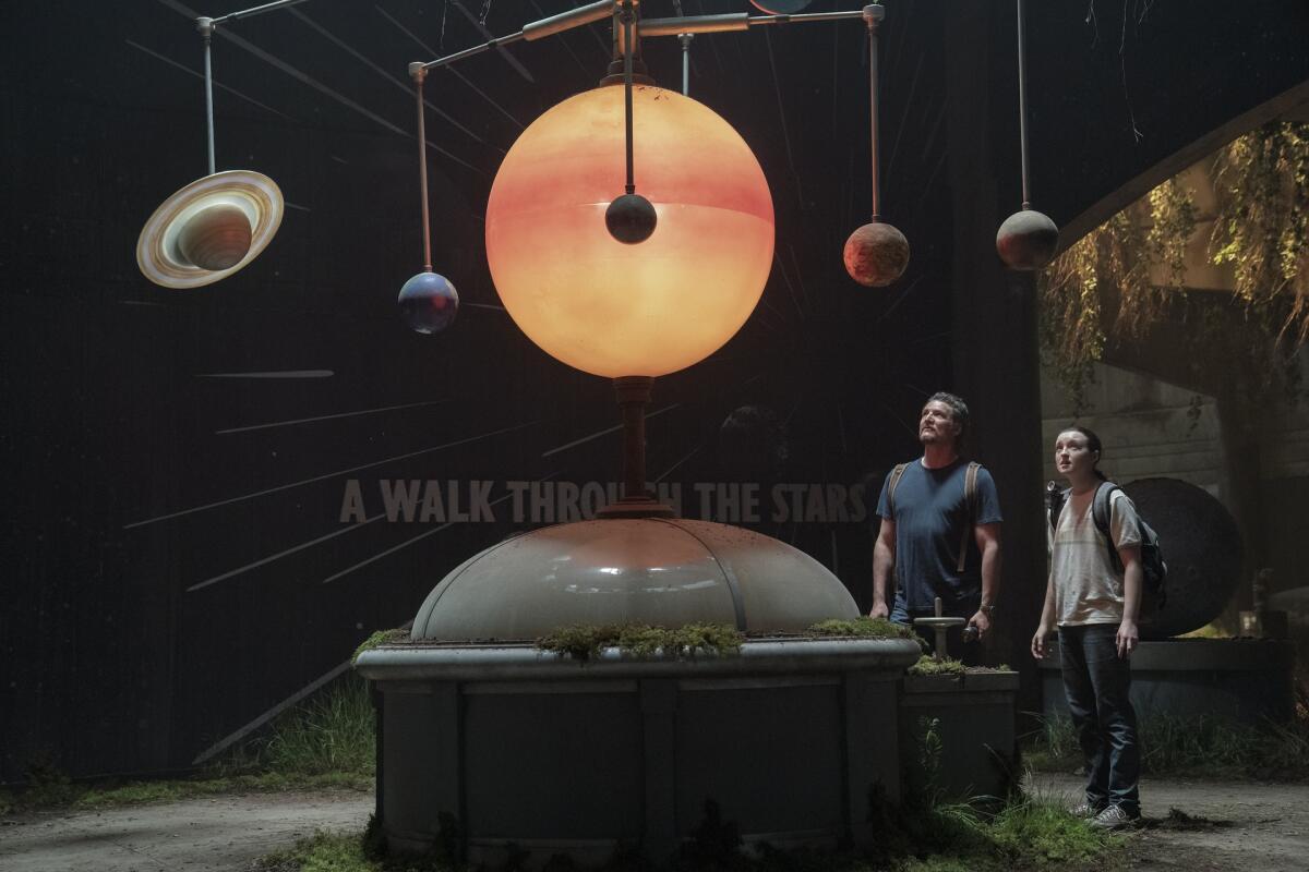 A solar system model hanging from a ceiling being stared at by a man and a teenage girl.