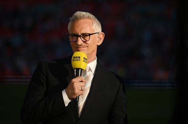 Gary Lineker in a black suit holding a yellow BBC sport microphone.