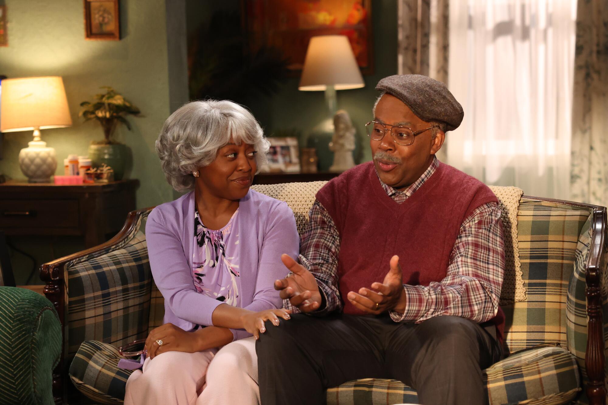 A woman in white haired wig sits next to a man dressed as an old man.