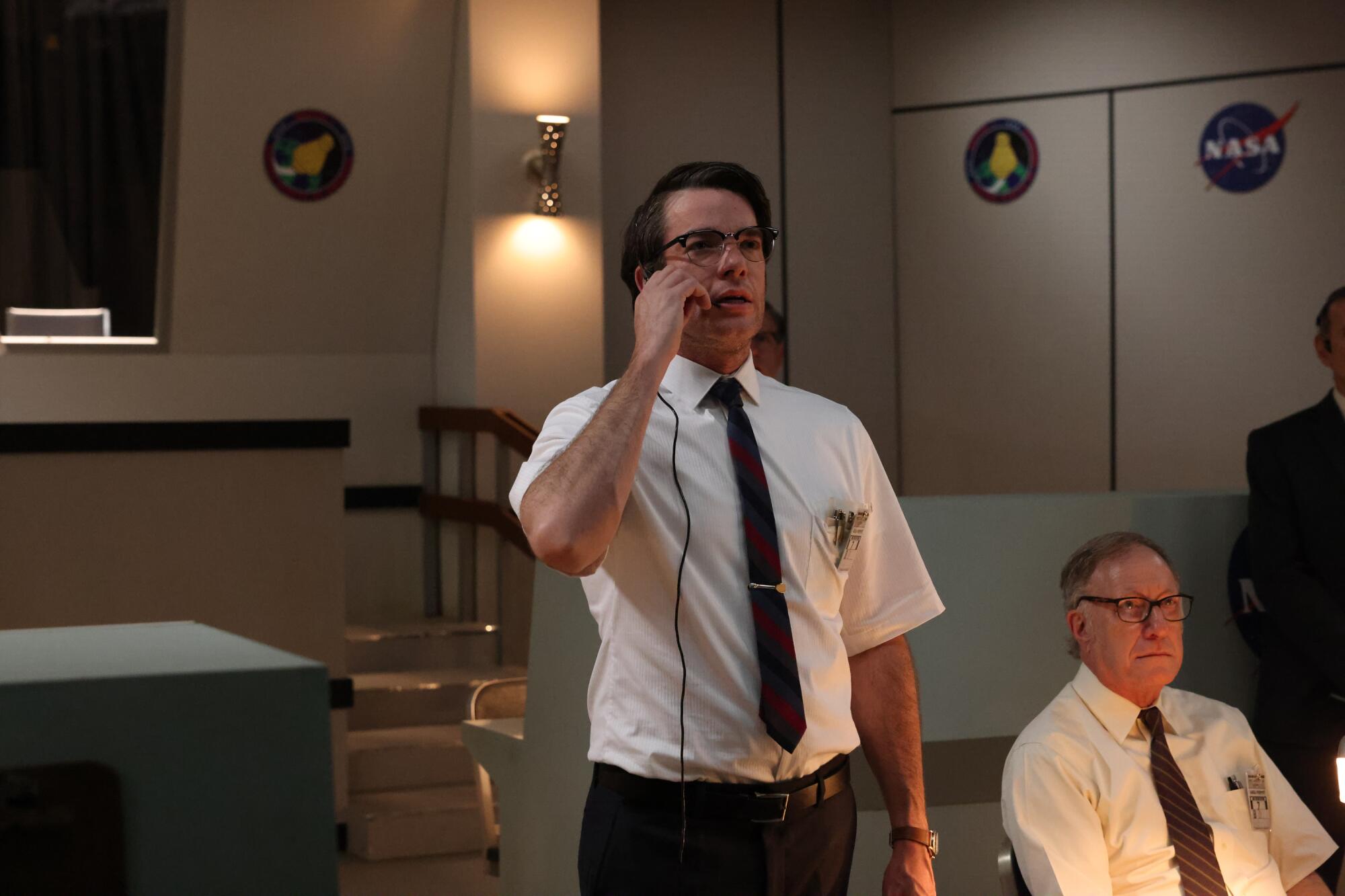 A man in glasses, a short-sleeve white shirt and red striped tie speaking into a headset.