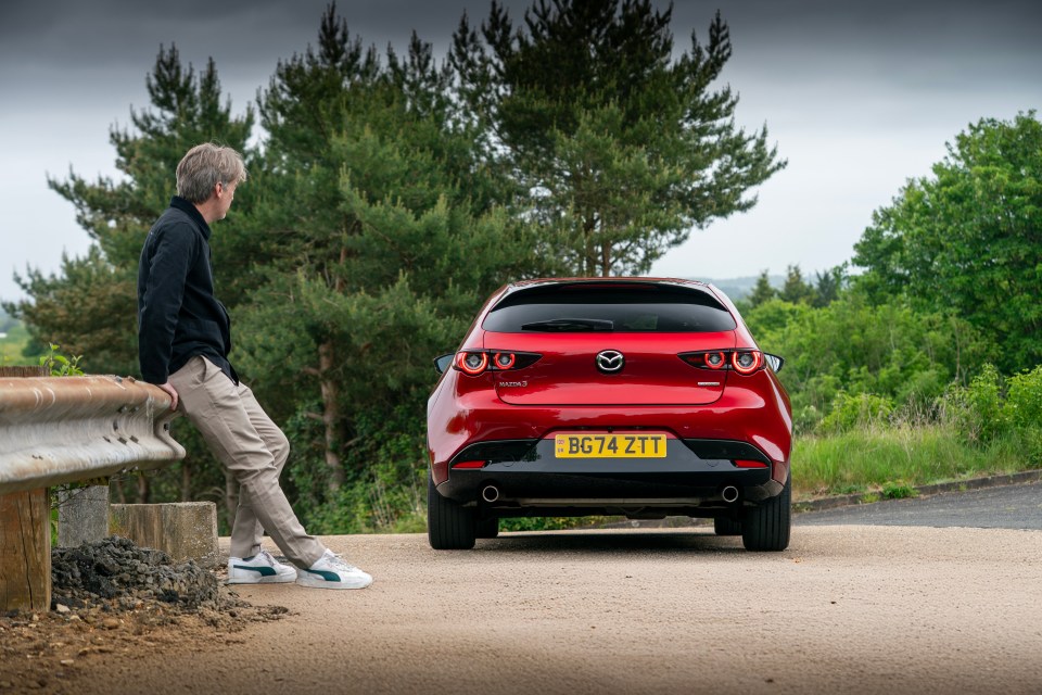 Man leaning on a railing looking at a red Mazda 3.