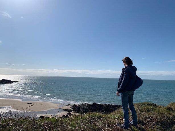 A tourist looks out at a sandy beach on a windy day