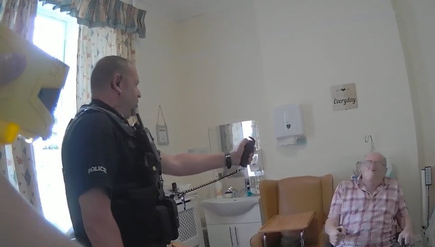 Still image from police bodycam footage showing a police officer aiming a taser at an elderly man in a care home.