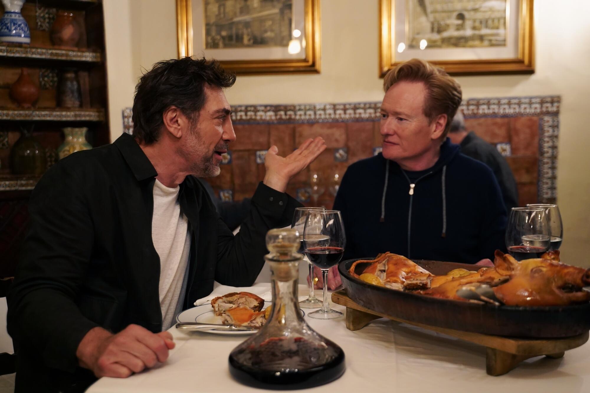Two men sit next to each other while having having a meal