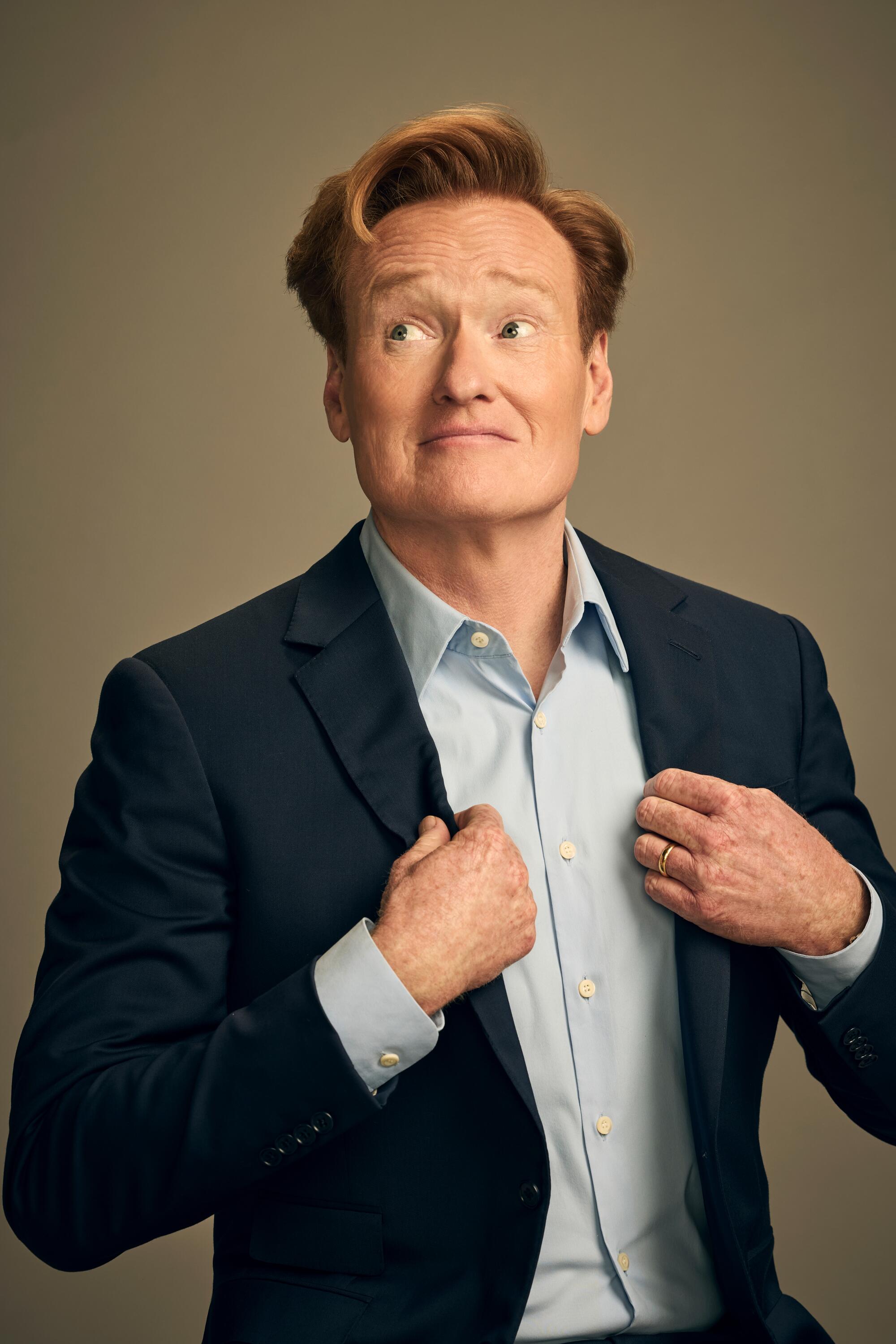A man in a navy suit poses for a photo with his hands adjusting his lapels