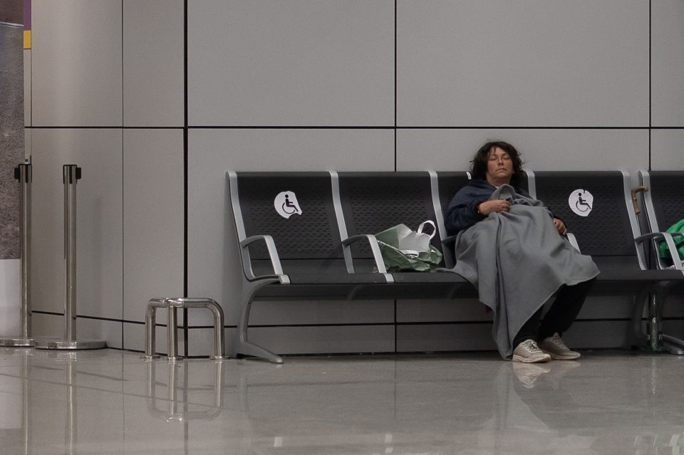 Homeless person sleeping on a bench at an airport.